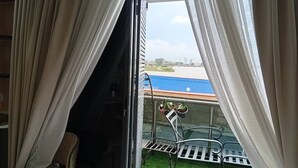 A room with a view of a body of water and a blue-roofed building. There is a chair and a table with chairs outside. - Casa De Lago - 2 bed luxury Lekki Phase 1, parking/secure/24/7 Electric (Lekki)