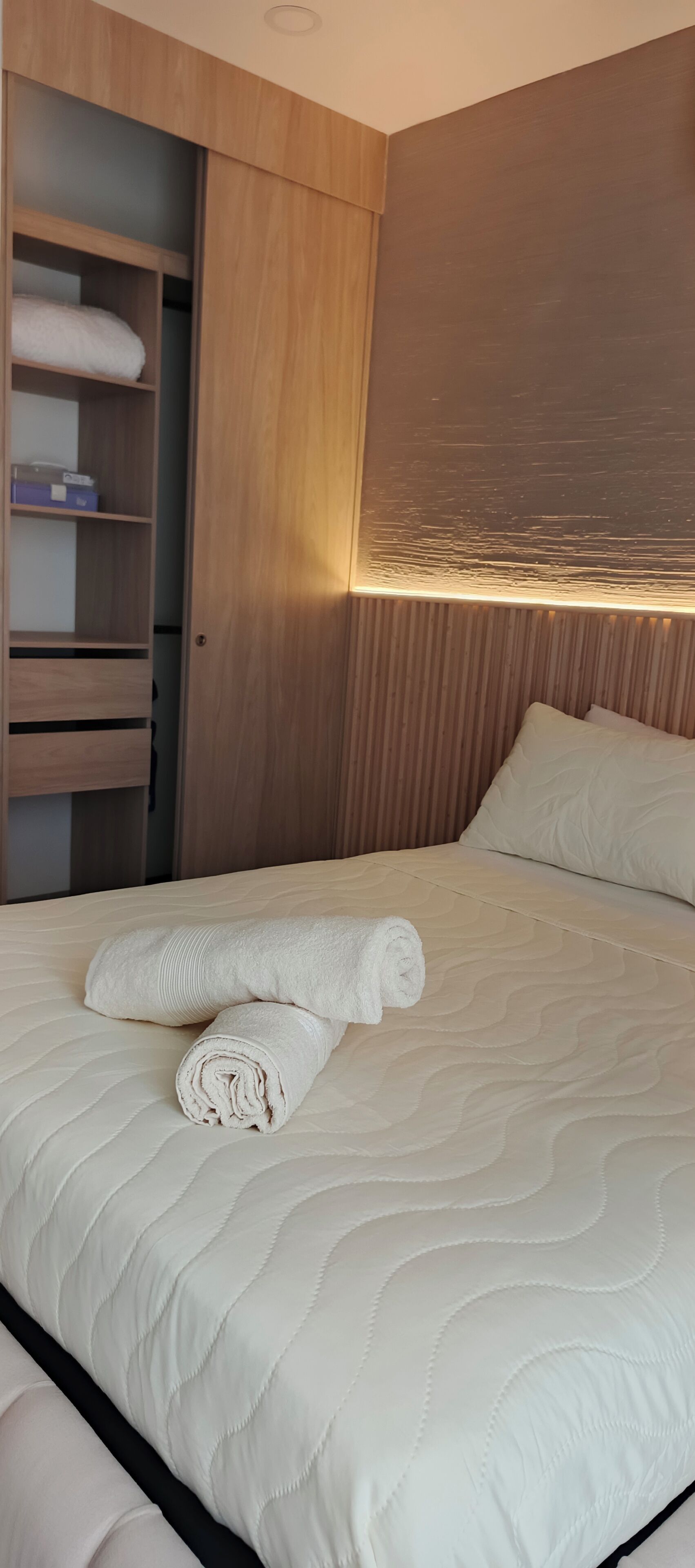 Ett hotellrum med en säng, en garderob i trä och en sänggavel med inbyggd belysning.