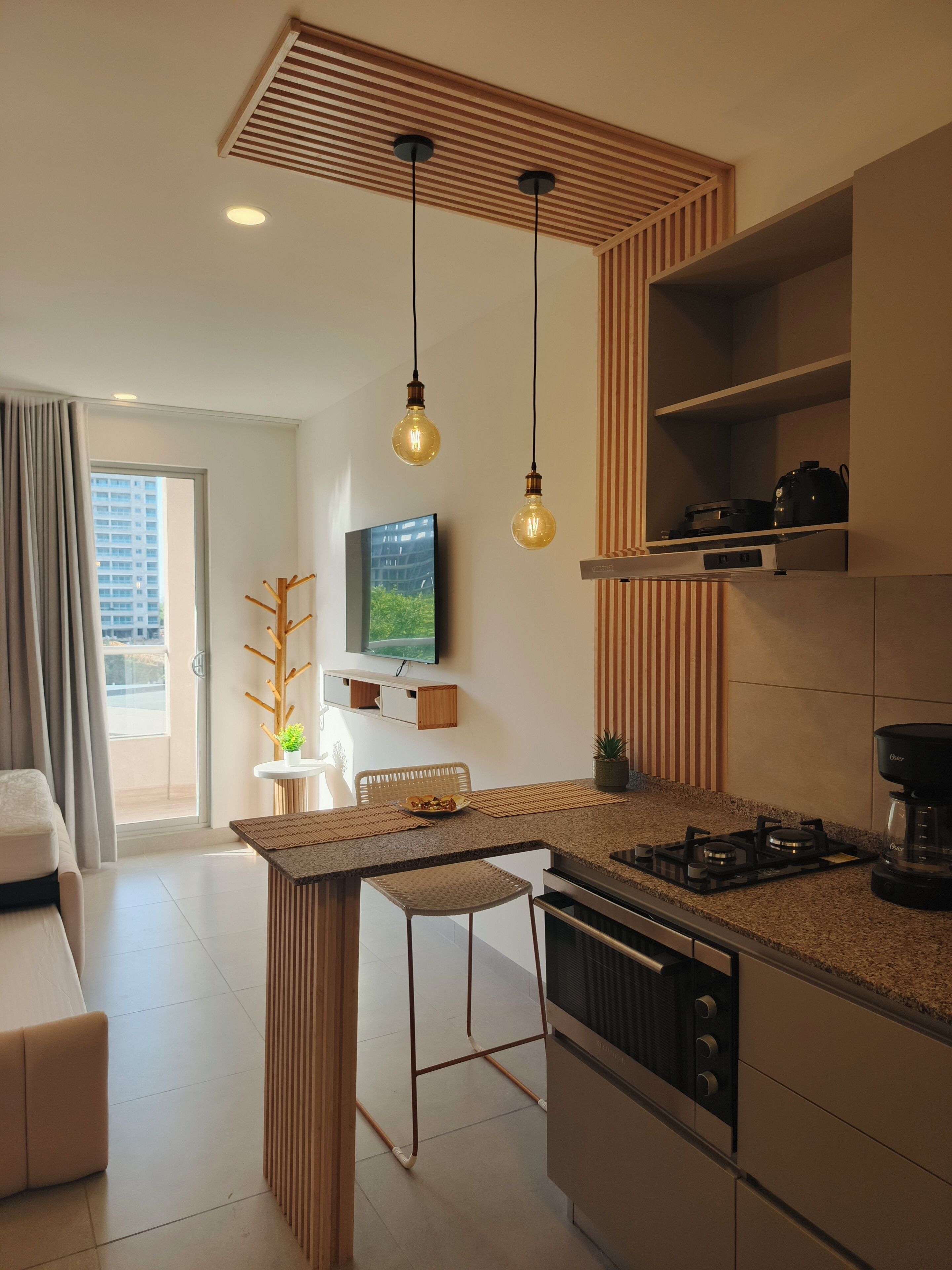 A modern kitchen with a central island, pendant lights, and a flat-screen TV.