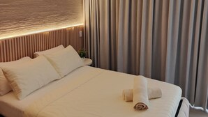 Una habitación de hotel con cama, aire acondicionado de pared, ventilador de techo y ventana con cortinas.
