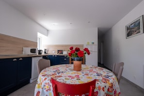Una cocina moderna con comedor, microondas, cafetera y un florero con flores rojas sobre una mesa.