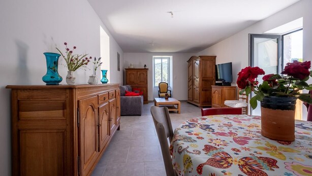 Ein geräumiger Raum mit einem Holzschrank, einem Sofa, einem Esstisch mit Blumenmuster und einem Fernseher auf einem Holzkasten.