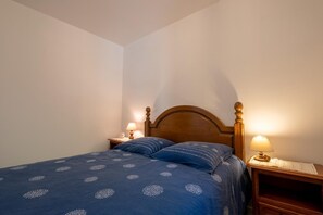 Een enkel bed met een houten hoofdbord, twee nachtkastjes met lampen, en een blauw beddegoed met patroon.