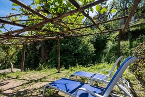 Ein überdachter Außenbereich mit zwei blauen Liegestühlen unter einer Holzpergola.