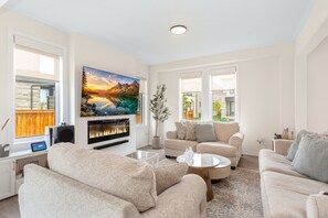 A modern living room with a fireplace, comfortable sofas, a flat-screen TV, and a large painting.