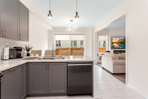 A modern kitchen with grey cabinets, a dishwasher, and pendant lighting.