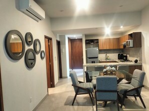 A modern kitchen with a dining area, featuring a glass table, chairs, and a kitchen island. - Welcoming 2-bedroom condo with Rooptop in vibrant Bucerías (Bucerías)