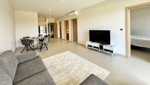 Moderni olohuone, jossa on sohva, taulutelevisio, ruokailutila tuoleineen ja taustalla keittiö.