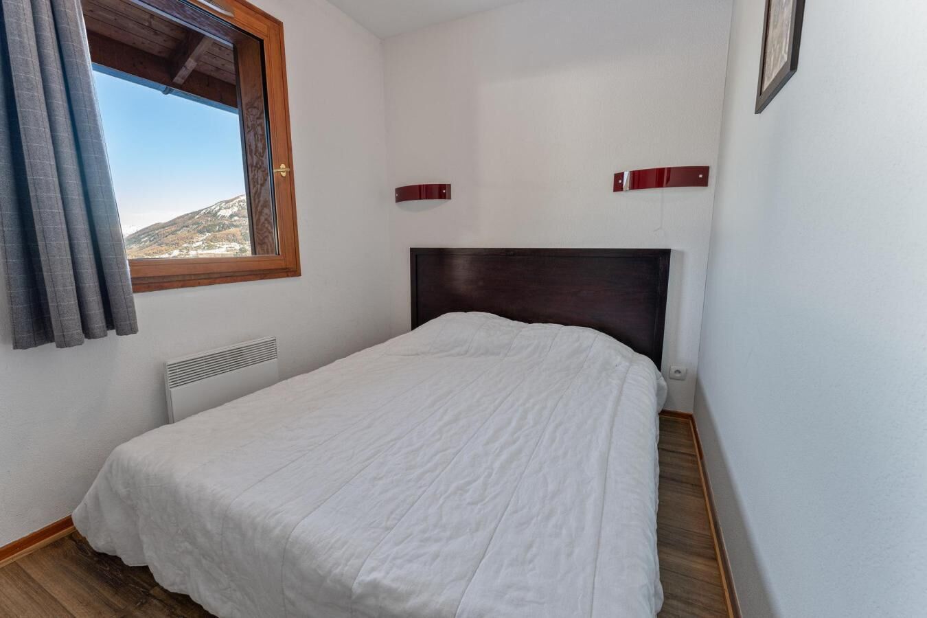 Une chambre avec un lit simple, une fenêtre avec des rideaux, un radiateur et une vue sur un paysage montagneux.