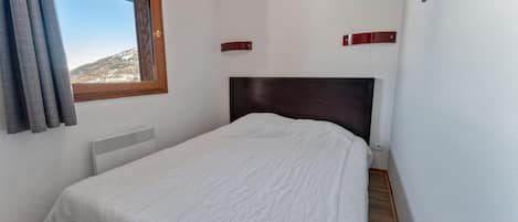 Un dormitorio con una cama individual, una ventana con cortinas, un radiador y vistas a un paisaje montañoso.