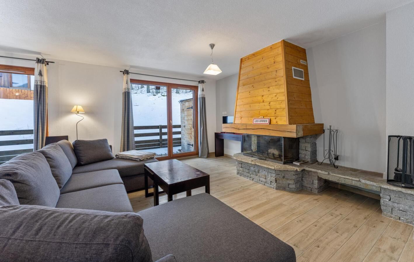 Un salon moderne avec une cheminée en pierre, un canapé, une table basse et une vue sur un paysage enneigé par de grandes fenêtres.