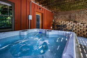 A hot tub with a stone wall backdrop, a wooden door, and a window.