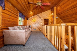 A log cabin interior with a sofa, ceiling fan, and a staircase.