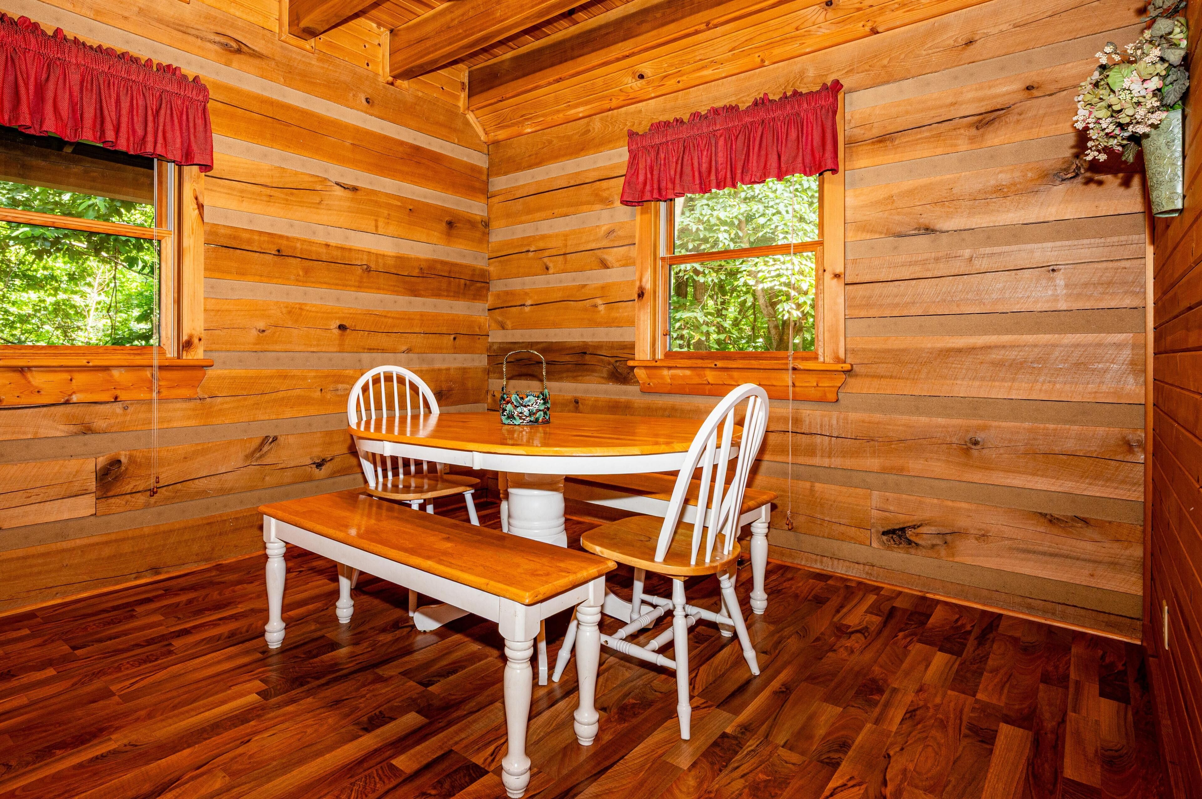 A wooden cabin interior with a wooden dining table, white chairs, and a bench.