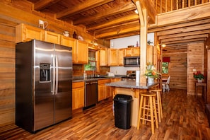 Ein Holzblockhaus-Interieur mit einem Edelstahlkühlschrank, Holzschränken, einer Mikrowelle und einer Bar mit Hockern.