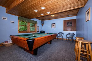 A pool table with a green felt surface, a television mounted on the wall, and two chairs. - Snuggled Inn | Private Brown County Log Cabin on 12 Wooded Acres (Bloomington)