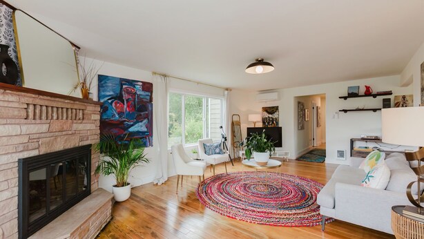 Un salon spacieux avec une cheminée, un grand tableau, un canapé, une table basse et un tapis coloré.