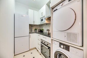 A compact kitchen with white cabinets, a built-in oven, a microwave, and a stacked washer-dryer unit. - LXR Parador (reformatted) 1 bedroom (Benalmádena)