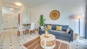 Een moderne woonkamer met een grijze bank, witte stoelen, een ronde salontafel en een kamerplant.