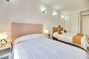 A hotel room with a large bed, a smaller bed, a nightstand with a lamp, a bedside table with a plant, and a wardrobe. - LXR Parador (reformatted) 1 bedroom (Benalmádena)