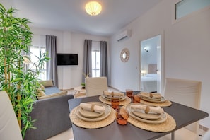 A modern hotel room with a dining area, a sofa, a television, and a large mirror. - LXR Parador (reformatted) 1 bedroom (Benalmádena)