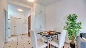 Een eetgedeelte met een tafel voor vier personen, witte stoelen, een potplant en een keuken op de achtergrond.
