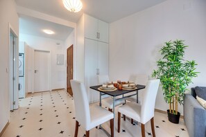 A dining area with a table set for four, white chairs, a potted plant, and a kitchen in the background. - LXR Parador (Reformatted) 1 Bedroom (Benalmádena)