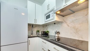 Een keuken met witte kastjes, een zwart aanrecht, een magnetron en een koffieapparaat.