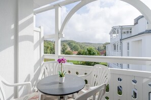 A balcony with a table and chairs, a potted plant, and a view of buildings and hills. - Lichtdurchflutete Ferienwohnung mit Balkon in Sudostlage in Sellin (Sellin)