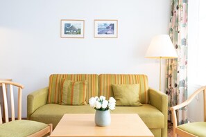 A room with a green sofa, a wooden table, and a vase with white flowers. There are two framed pictures on the wall. - Lichtdurchflutete Ferienwohnung mit Balkon in Sudostlage in Sellin (Sellin)