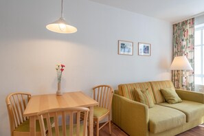 A room with a dining table, chairs, a sofa, a lamp, and two framed pictures on the wall. - Lichtdurchflutete Ferienwohnung mit Balkon in Sudostlage in Sellin (Sellin)