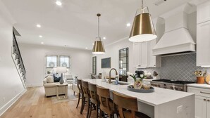 Una cucina moderna con isola centrale, sgabelli da bar, illuminazione a sospensione e una scala che conduce a una zona living.