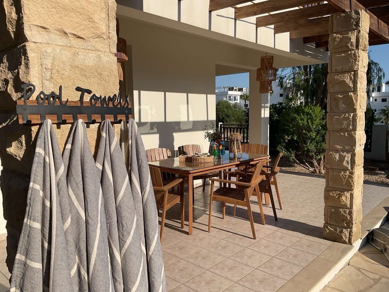 An outdoor patio with a wooden table and chairs, a stone pillar, and a hanging towel rack.