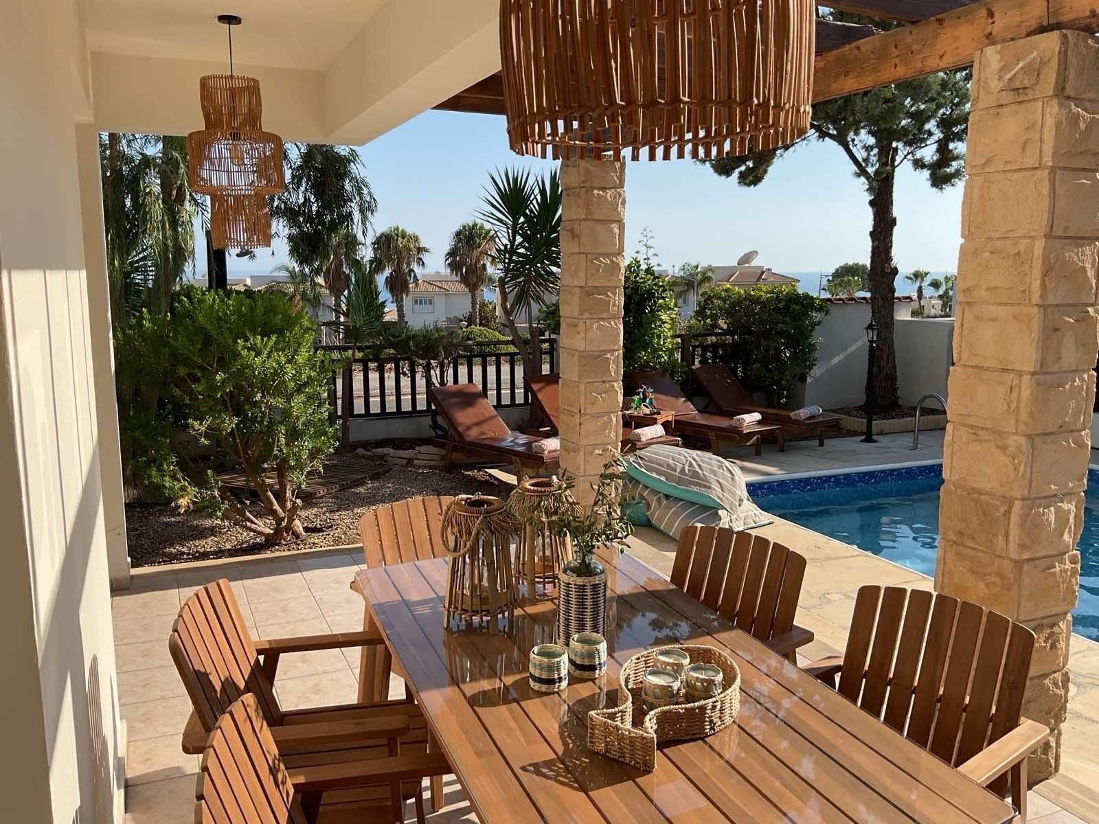 A wooden poolside area with lounge chairs, a table with chairs, and a hanging light fixture.