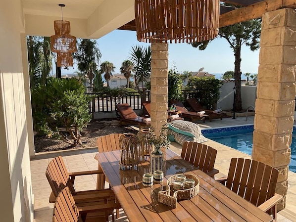 A wooden poolside area with lounge chairs, a table with chairs, and a hanging light fixture.
