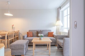 Ein Wohnzimmer mit einer Couch, zwei Sesseln, einem Couchtisch, einem Esstisch mit Stühlen und einer Vase mit Blumen.