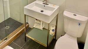 A bathroom with a glass shower enclosure, a white sink with a gold-colored vanity, a mirror with a gold light fixture, and a white toilet.