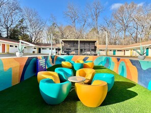 A colorful outdoor seating area with a pool, surrounded by a building with a unique mural design. - Boutique Hotel | 1 Bedroom Suite w/ Full Kitchen (Starkville)
