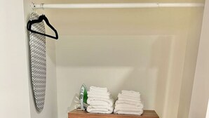 A wooden dresser with drawers, a hanging garment on a rack, and a stack of folded towels.