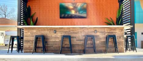A modern bar area with a wooden ceiling, a large abstract painting, and several stools.