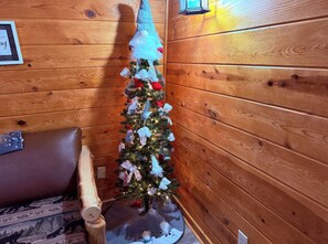 Ein Holzblockhaus-Innenraum mit geschmücktem Weihnachtsbaum, einem braunen Ledersofa und einer Holzwand.