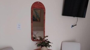 Une pièce avec un téléviseur fixé au mur, une table ronde en bois ornée d’une plante, et deux chaises blanches.