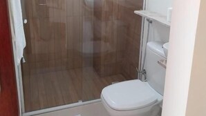 Une salle de bain avec une douche à parois de verre, des toilettes blanches et un petit lavabo.
