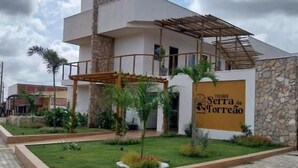 Un bâtiment moderne avec une façade en pierre, une enseigne indiquant « Serra de Torredeo », et un espace d’entrée pavé agrémenté d’une bande de revêtement tactile jaune.