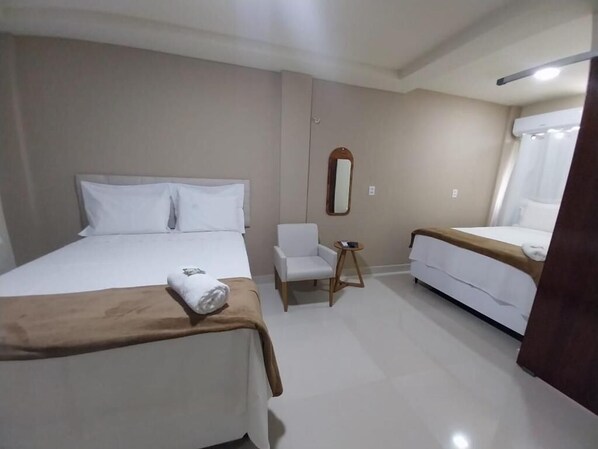 Une chambre d’hôtel avec un grand lit, un lit plus petit, une chaise et un miroir au mur.