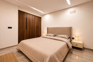 A bedroom with a bed, nightstands, a wooden wardrobe, and recessed ceiling lighting. - Modern Living in Soukra (Ariana)