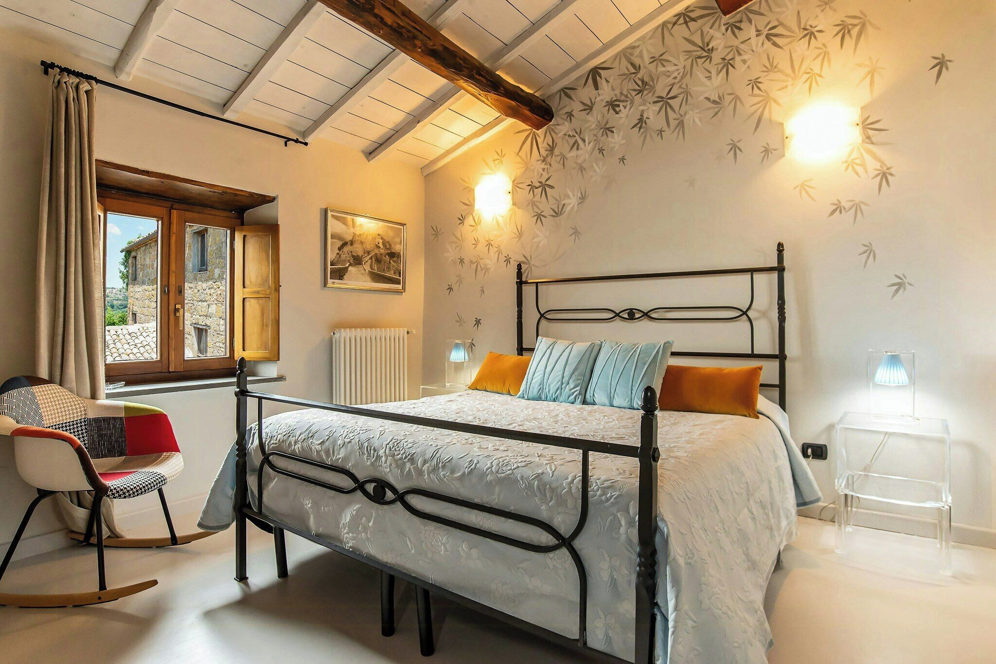 Ein Schlafzimmer mit Bett, Schaukelstuhl, Fenster und Wandleuchte.