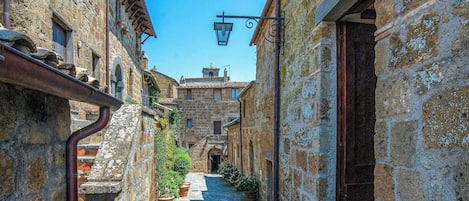 Un estrecho callejón empedrado flanqueado por edificios, con un cielo azul despejado y un farol.