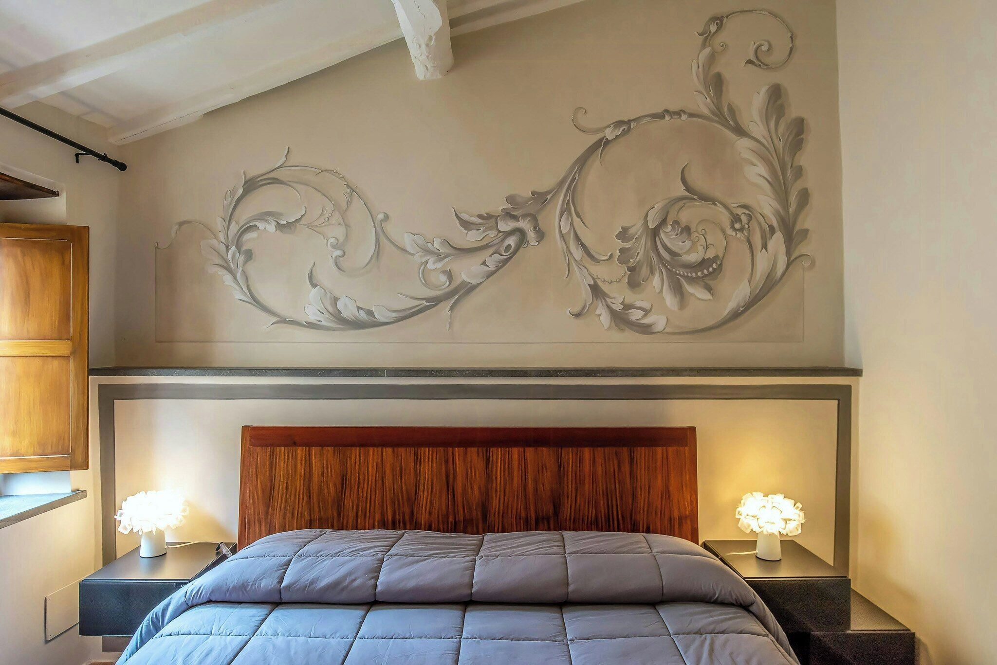 Une chambre à coucher avec un grand lit, deux tables de chevet avec des lampes, une fresque murale décorative et une tête de lit en bois.