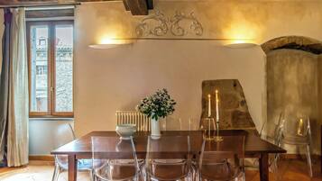 A dining area with a wooden table, clear chairs, a vase with flowers, and a stone fireplace.